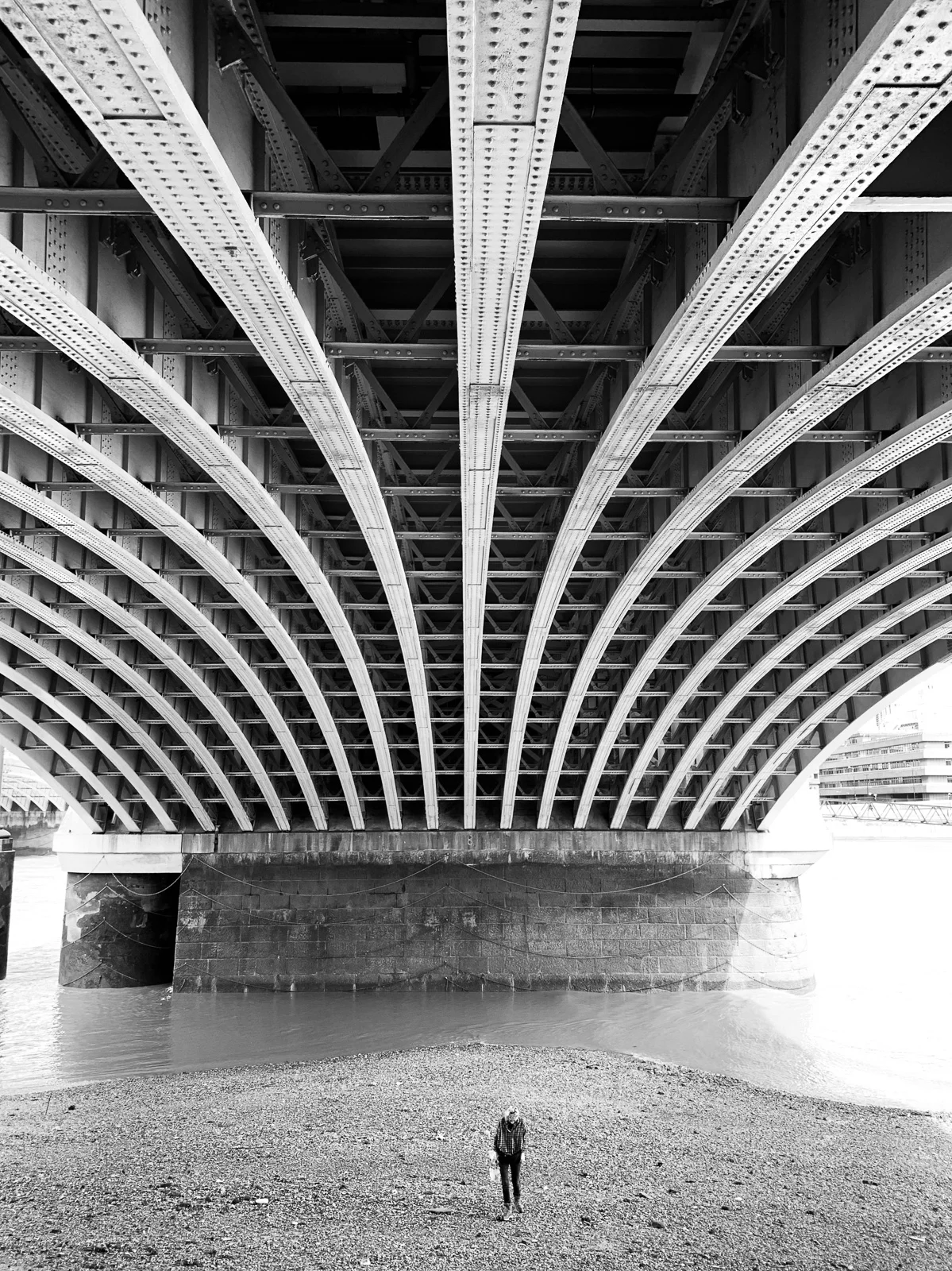 A solitary figure beneath the repeating curves of a bridge. Photograph by Adelina Persa.