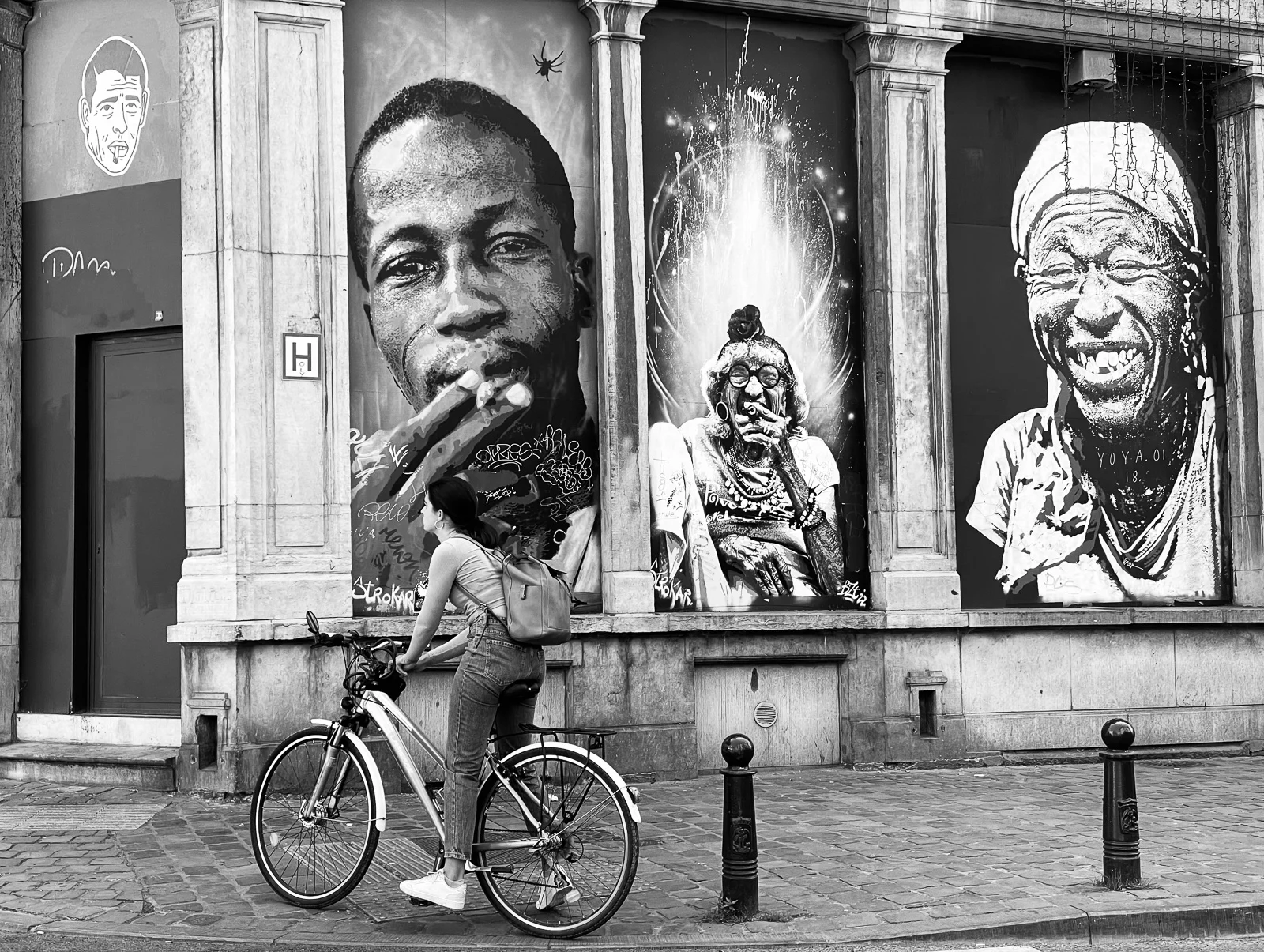 A cyclist passing portraits displayed on a building. Photograph by Adelina Persa.